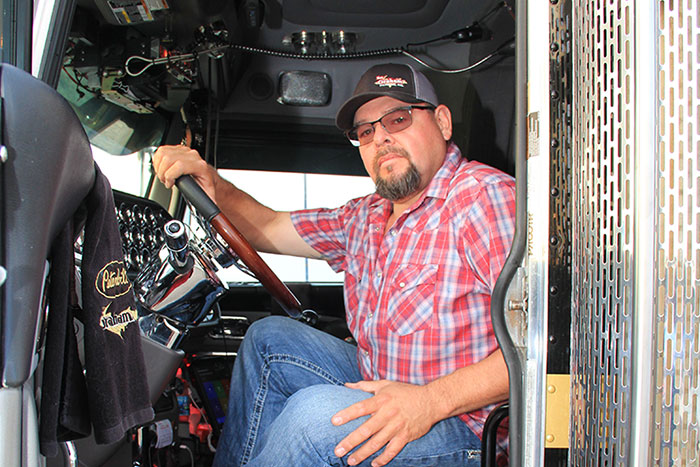 Truck driver sitting in a cab with hand on wheel.