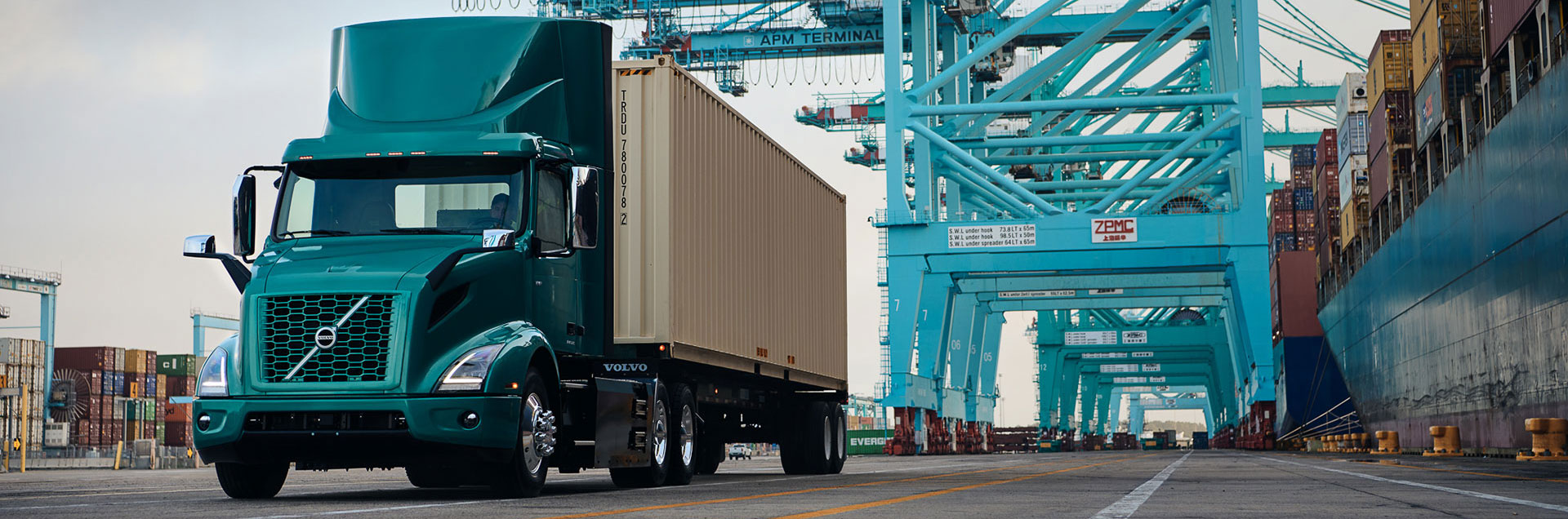 Metallic green Volvo VNR Electric truck at a shipping port terminal, representing zero-emission electromobility for sustainable drayage, local distribution, and regional hauling with up to 275 miles of range.