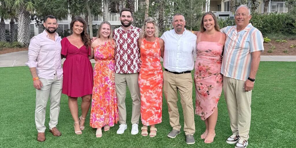 JX Truck Center team members and guests smiling together outdoors at the Peterbilt Legends Circle event on Amelia Island.