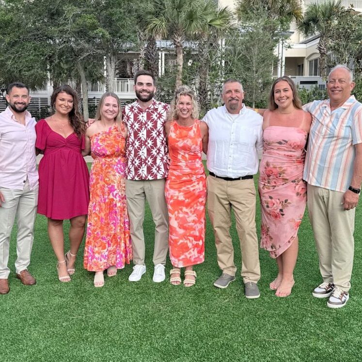 JX Truck Center team members and guests smiling together outdoors at the Peterbilt Legends Circle event on Amelia Island.